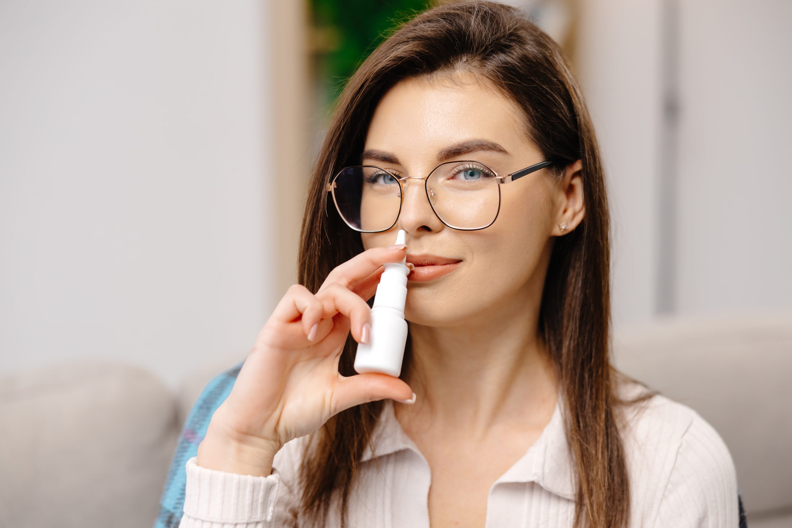 Woman wearing glasses using a nasal spray inhaler