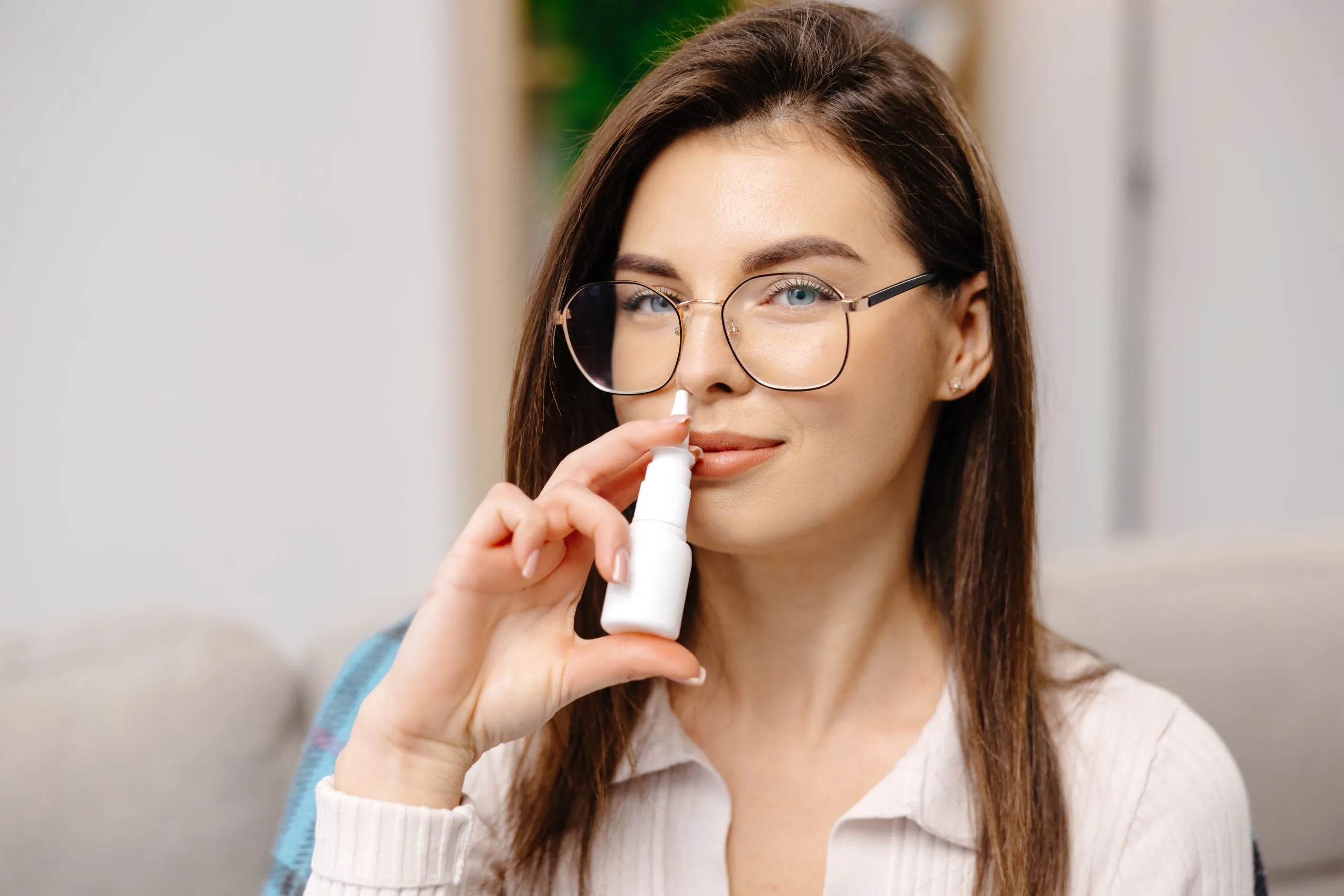 Woman wearing glasses using a nasal spray inhaler