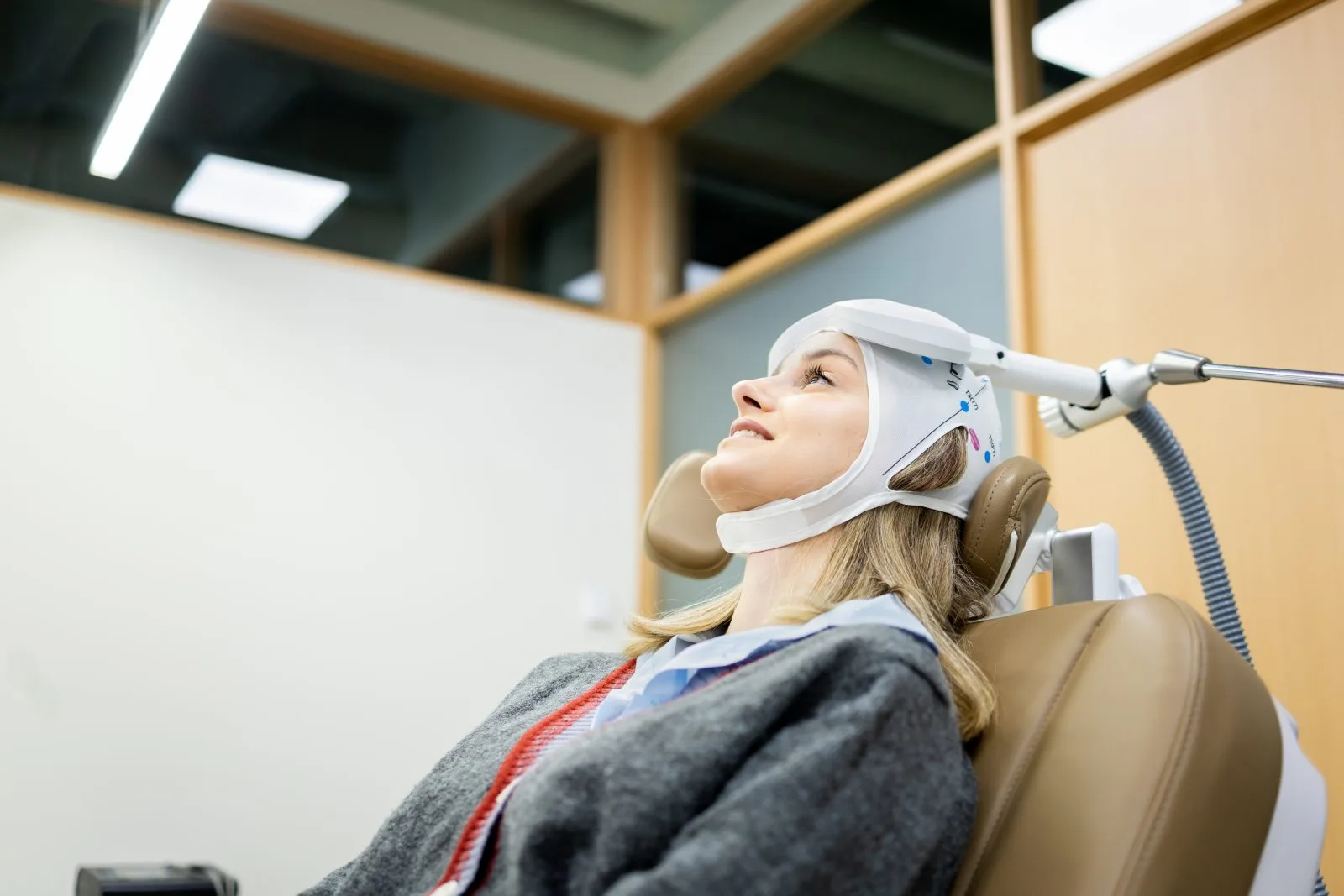 Patient receiving TMS therapy with magnetic coil helmet positioned on head during treatment session