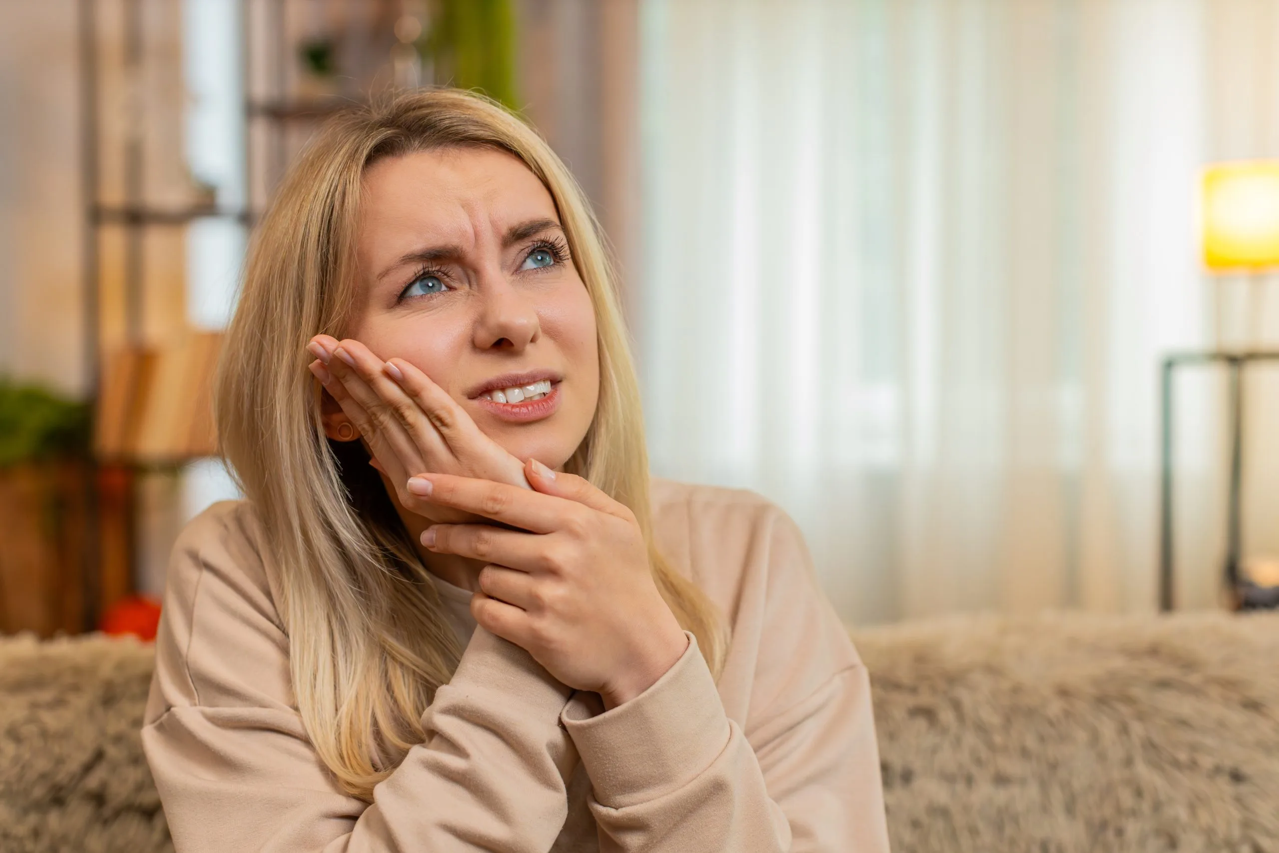 Woman holding her cheek in discomfort while sitting on a couch