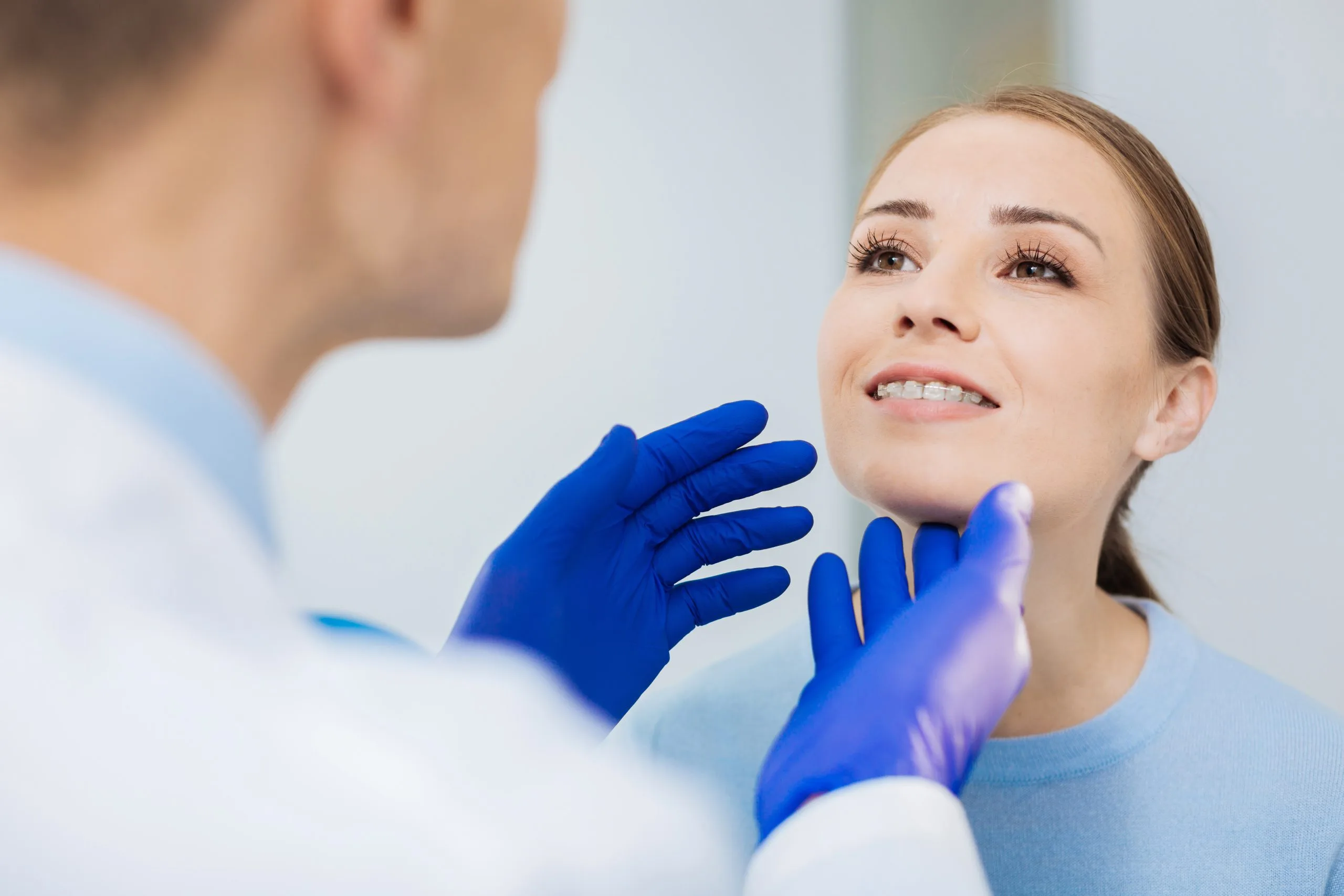 Young woman tilting her chin up while a clinician in blue gloves examines her mouth
