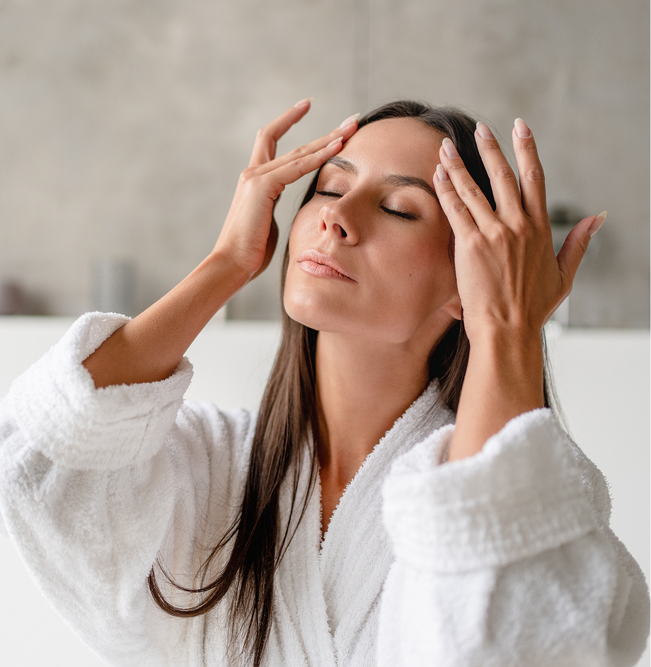 Woman in white robe touching her forehead and temples with eyes closed