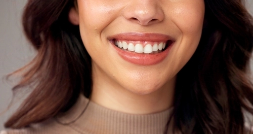 Woman smiling broadly, showing bright white teeth against neutral studio background