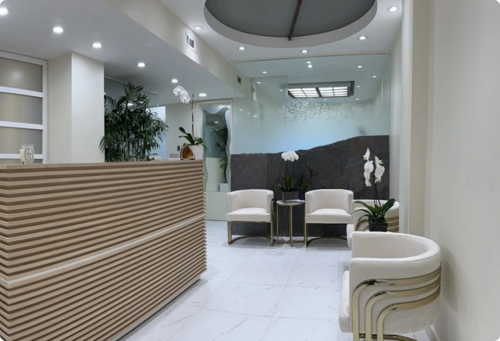 Modern reception area with striped wood desk, white seating, marble flooring, and potted plants at Cosmetic Dental Studios