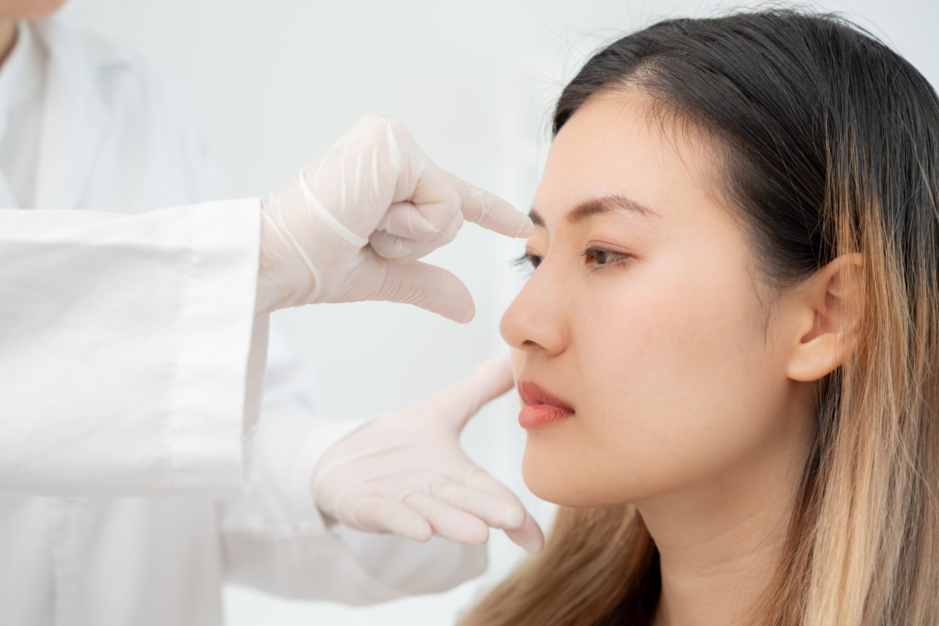 Cosmetic surgeon in gloves examining patient's nose profile for aesthetic assessment