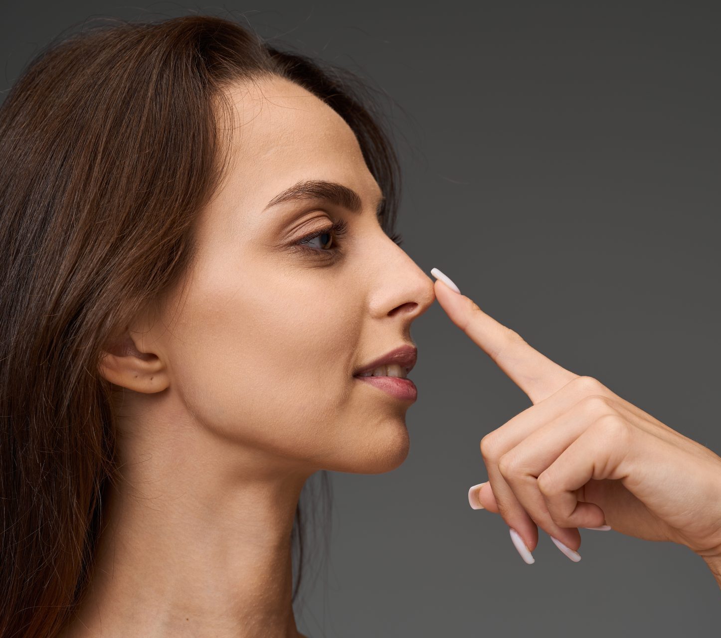 Woman in profile pointing to her nose, considering rhinoplasty