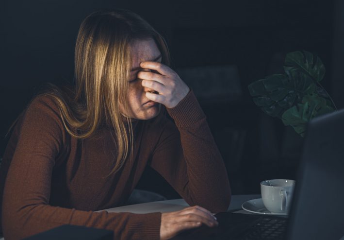 A young woman is working at a computer at night, holding a cup of coffee in her hands, wants to sleep.