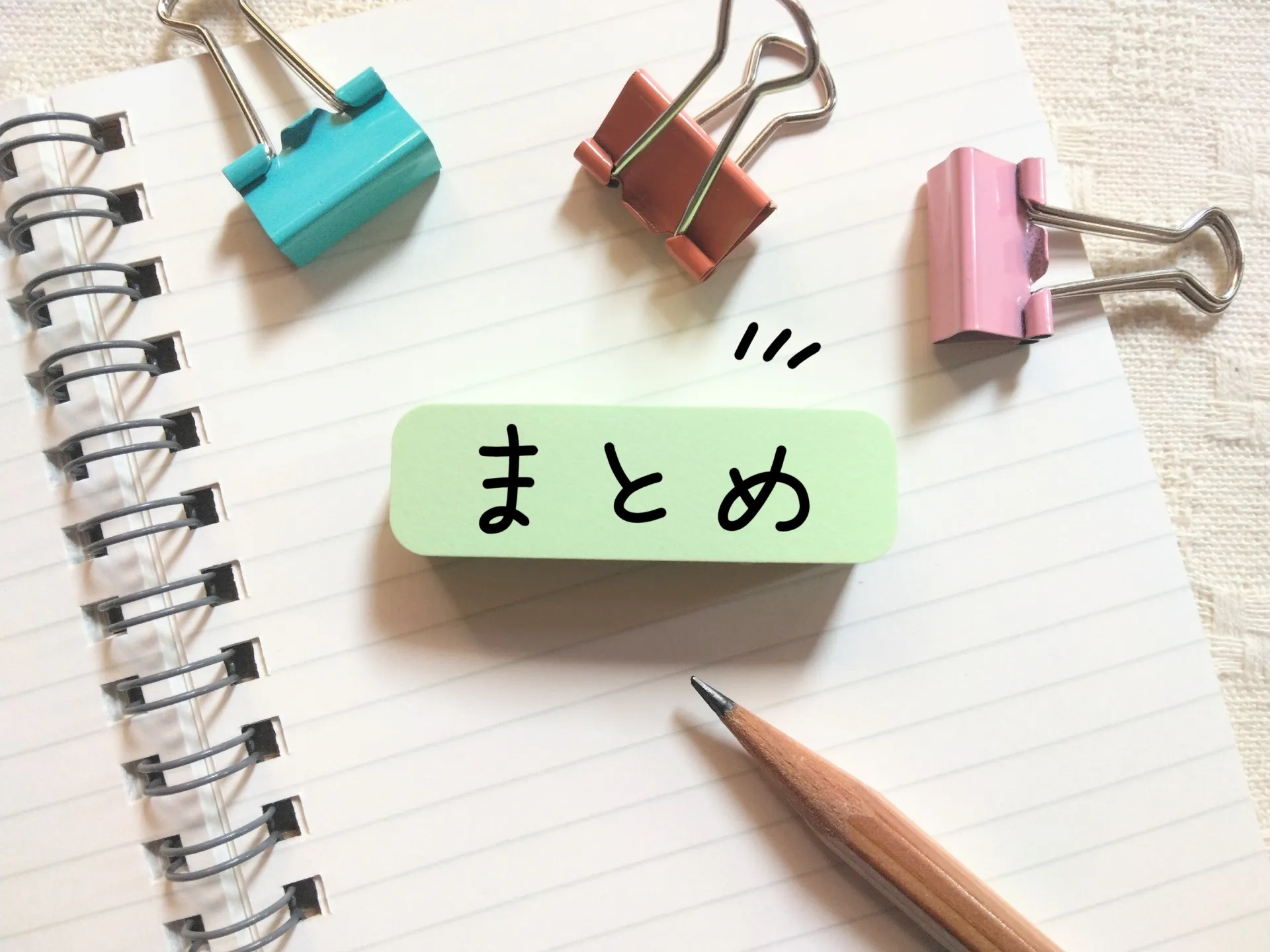 ノートに「まとめ」と書かれた付箋、クリップ、鉛筆