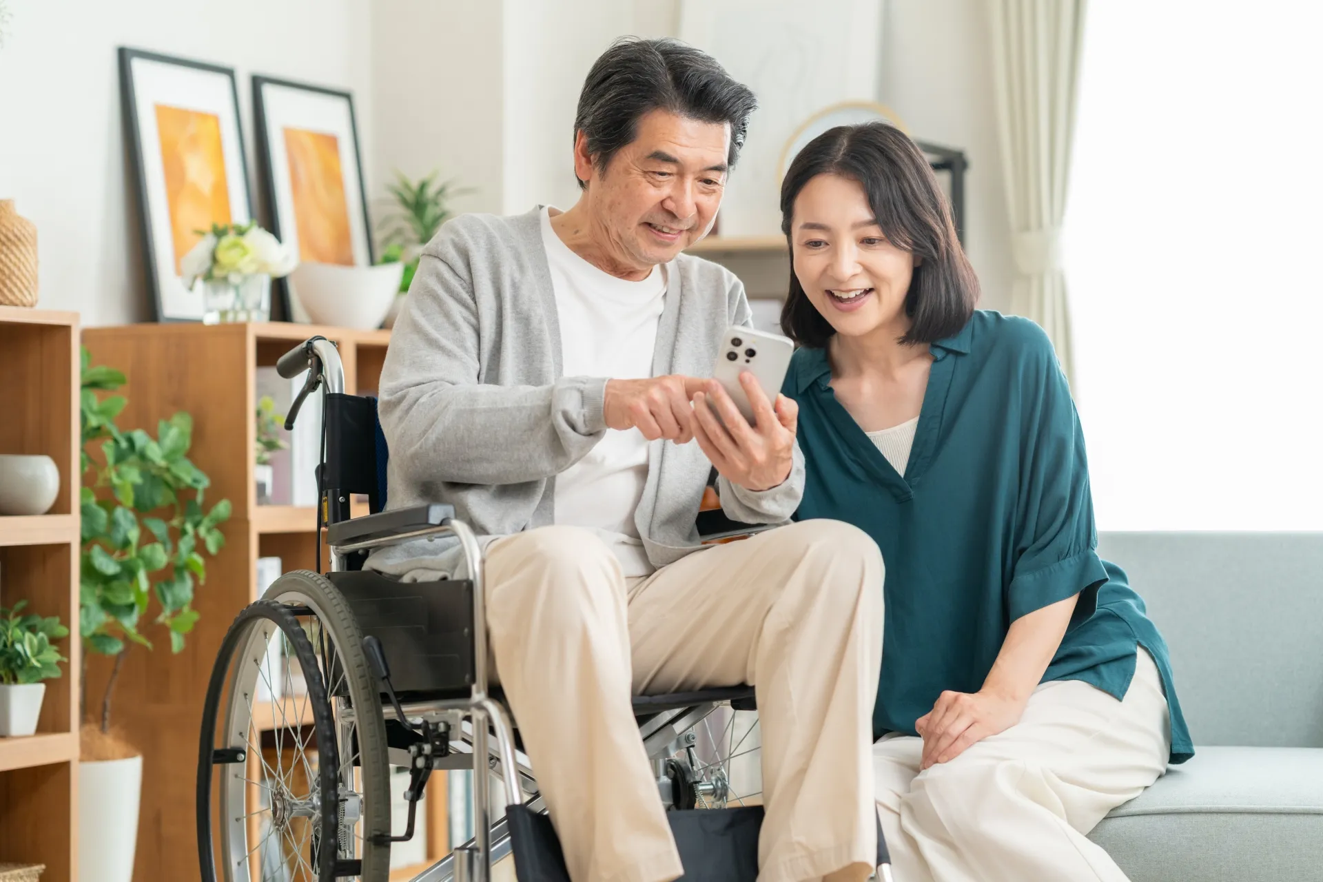 リビングで車椅子の夫のスマホを一緒に観る妻