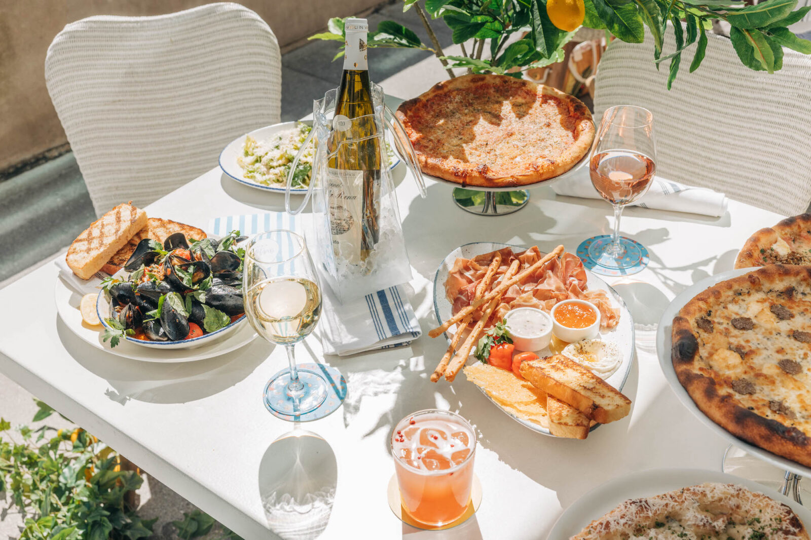 Table spread of Prosciutto San Daniele, Black Truffle and Three Cheese pizza, Bar Harbor Mussels with bottles and poured glass of wine.