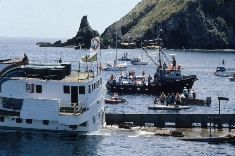 The original Rainbow Warrior half submerged in water, with people on small craft looking on