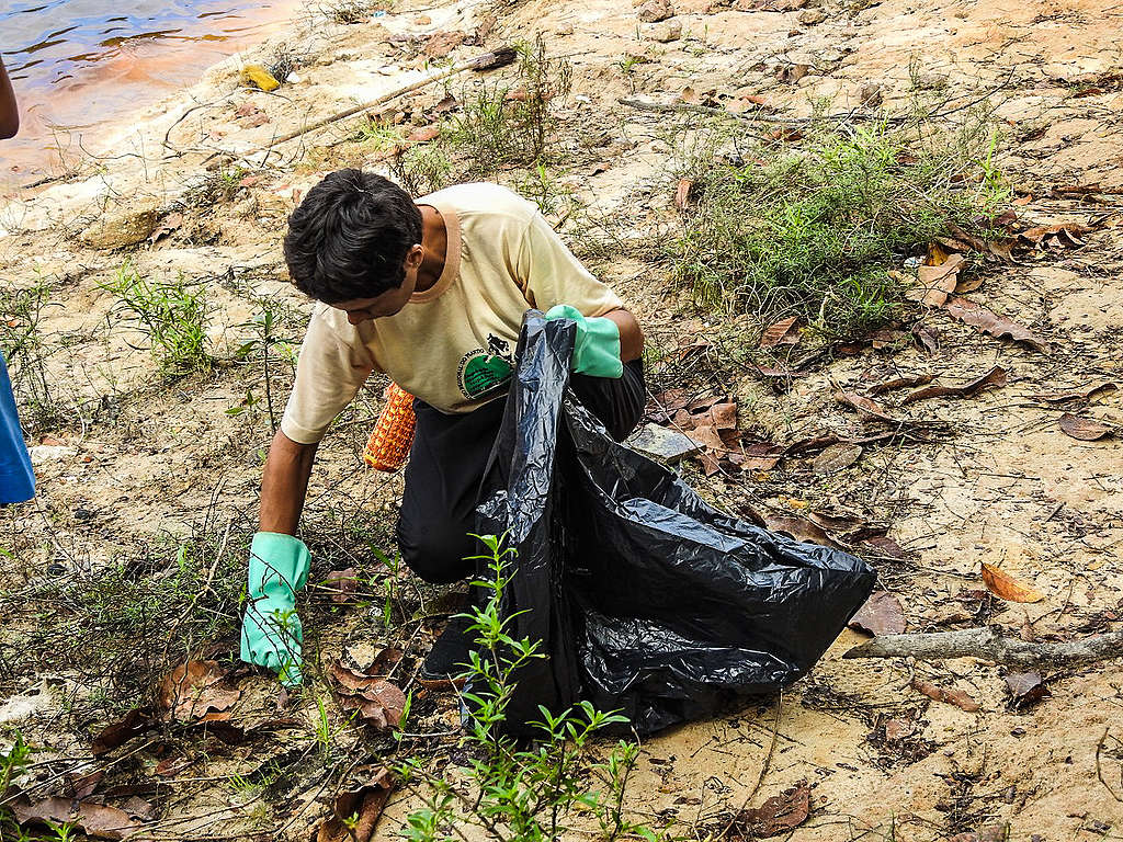 Voluntário recolhe lixo em ação de limpeza na praia de Tarumã (AM).