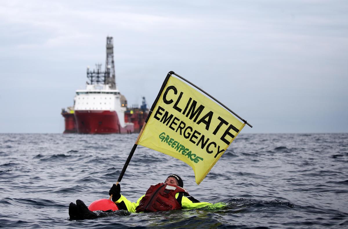 Ativista Sarah North nas águas frias do Mar do Norte com o cartaz "Emergência Climática". © Greenpeace