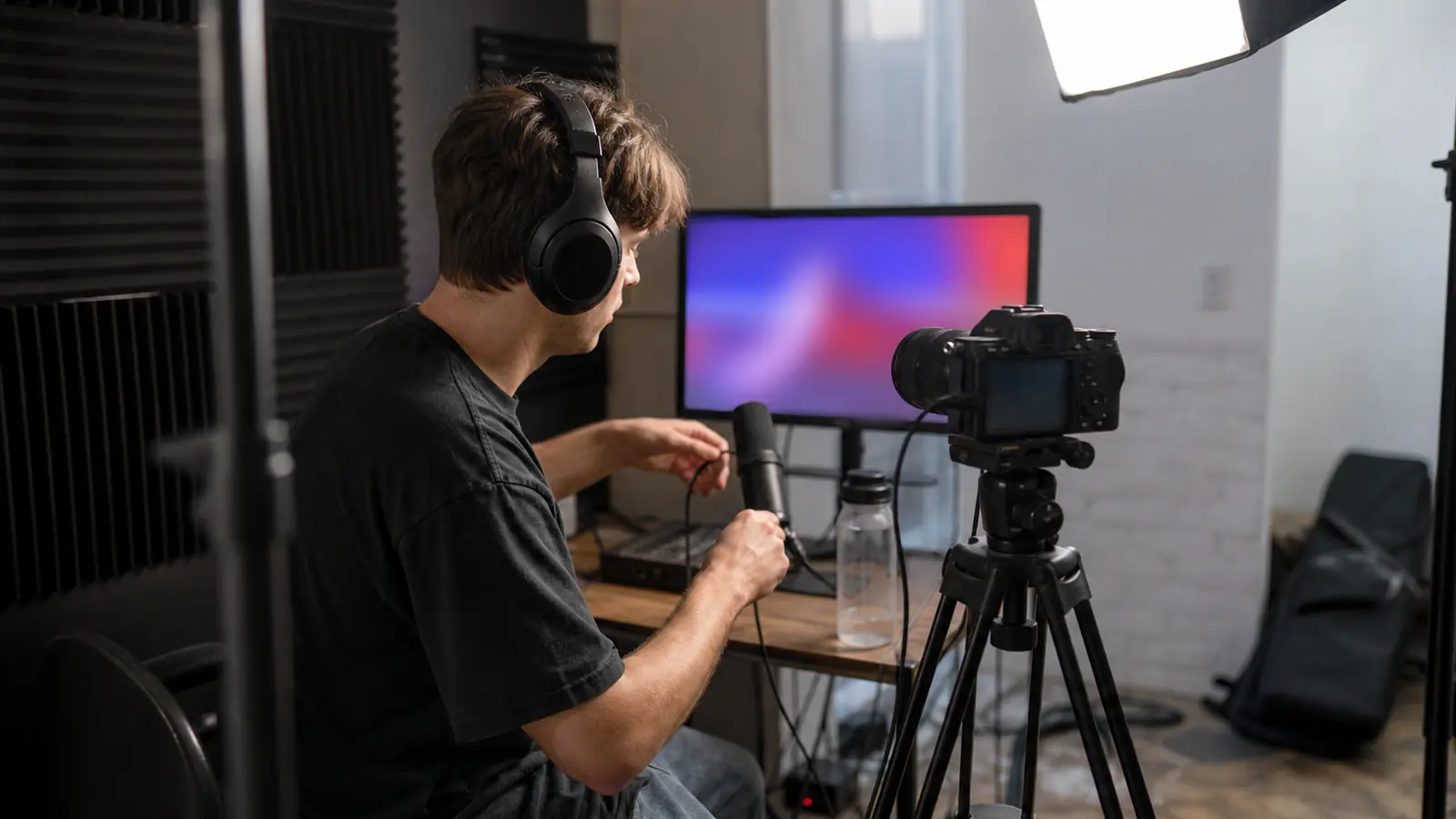 Ein nicht identifizierbarer Creator richtet in einem kleinen Studio Mikrofon, Kopfhörer und Kamera für eine Gaming-Kampagne ein.