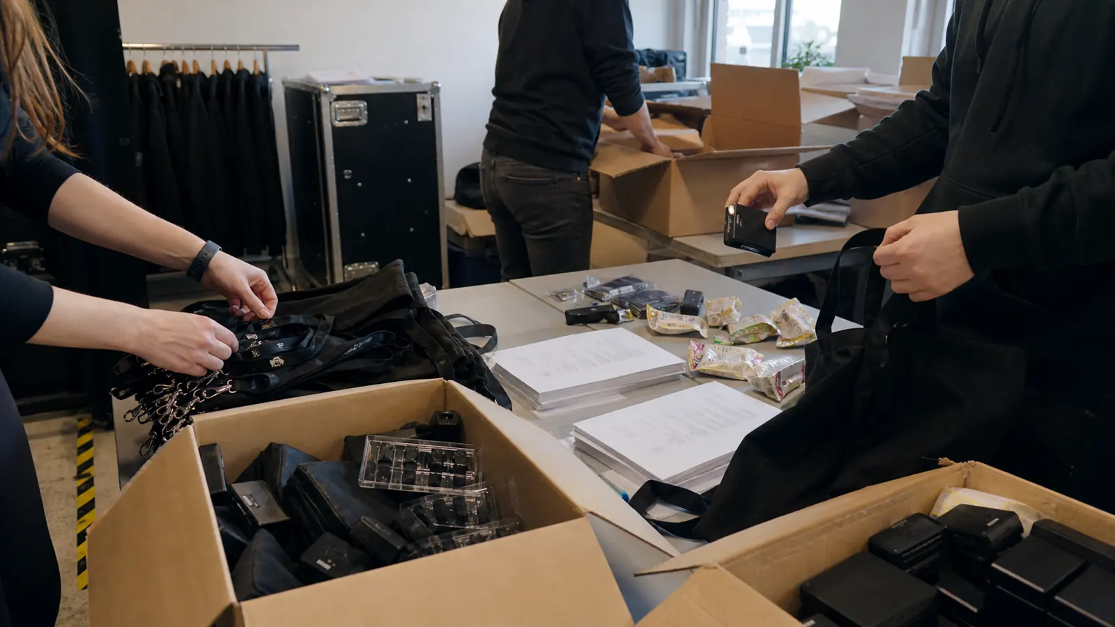 Mehrere nicht erkennbare Personen sortieren neutrale Event-Kits, Lanyards, Akkus und Unterlagen für eine Creator-Aktivierung.