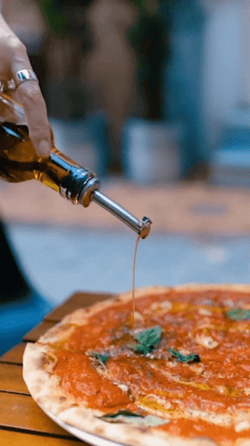 User-generated content of olive oil drizzle on pizza with fresh basil used for video marketing