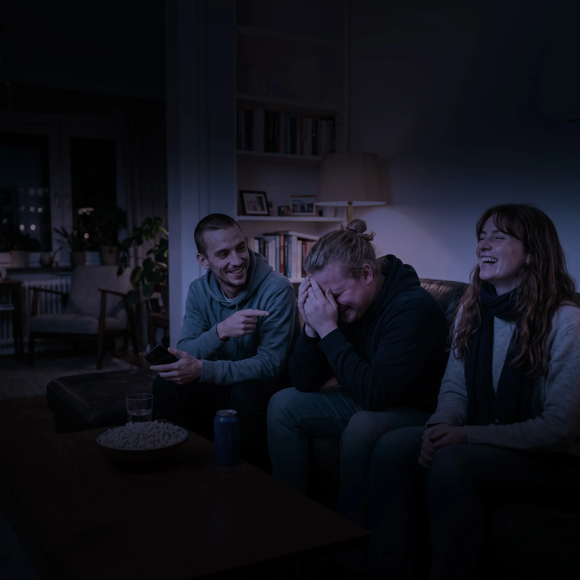 Le soir dans un salon, trois potes sur un canapé : l'un, téléphone en main, pointe du doigt son voisin qui se cache le visage, pendant que leur amie éclate de rire