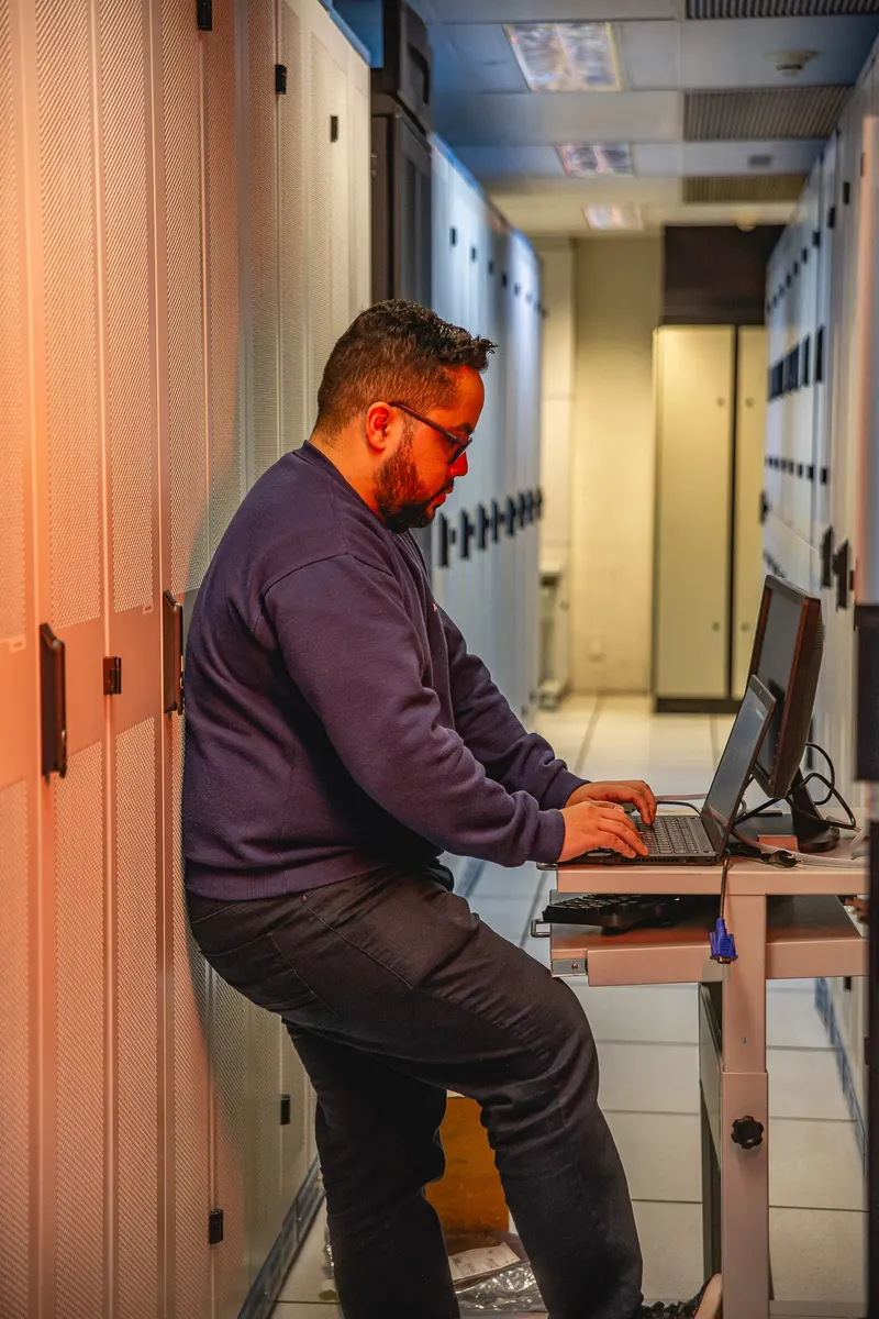 Especialista da Adentro com notebook ao lado dos racks do data center