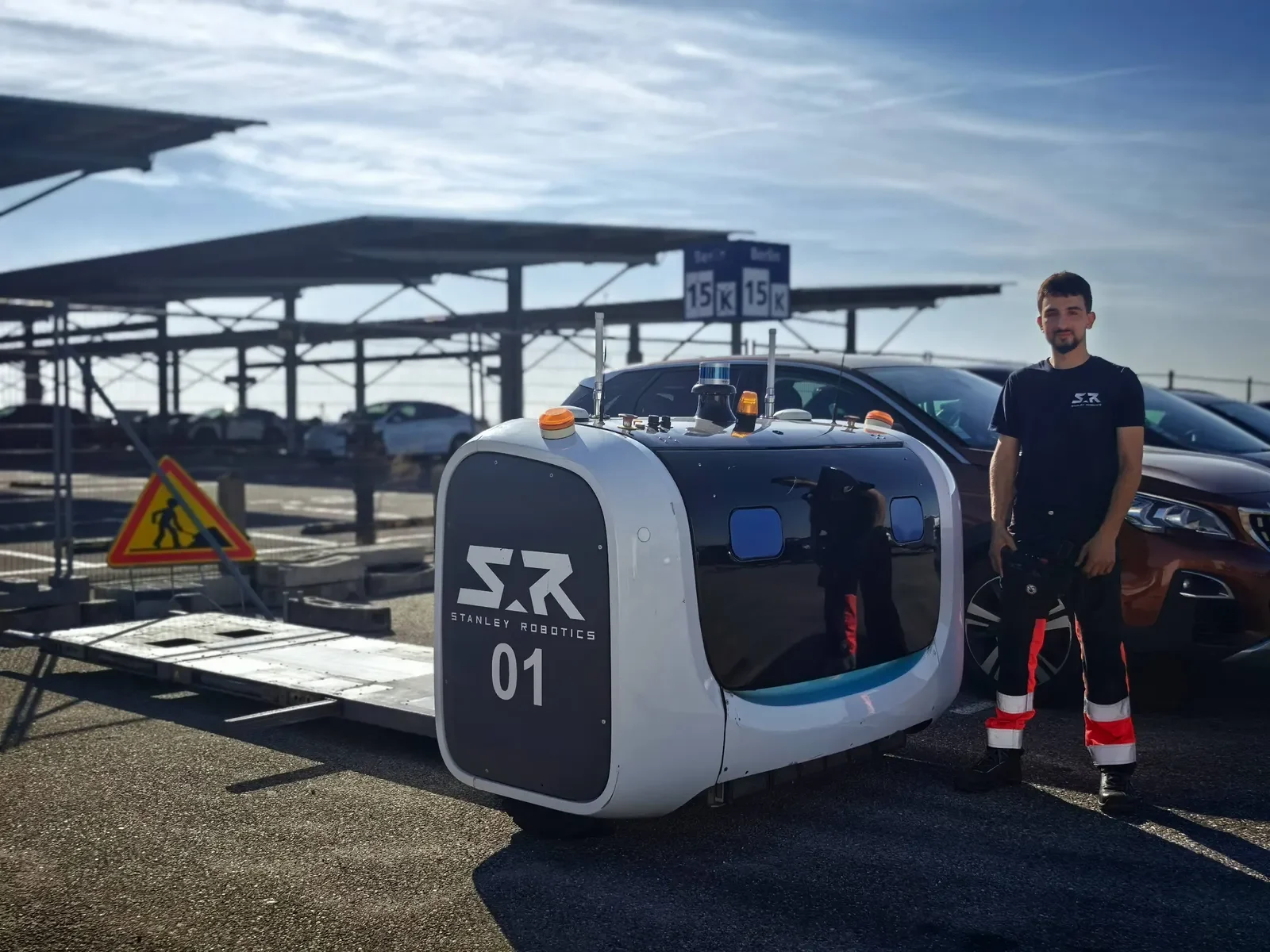 A Stanley Robotics technician beside a STAN robot on an outdoor parking site