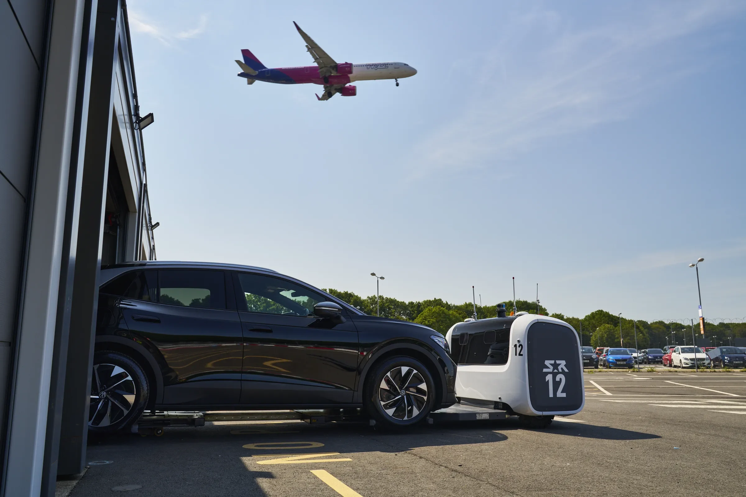A Stanley Robotics STAN robot moving a passenger car at London Gatwick as a plane takes off overhead
