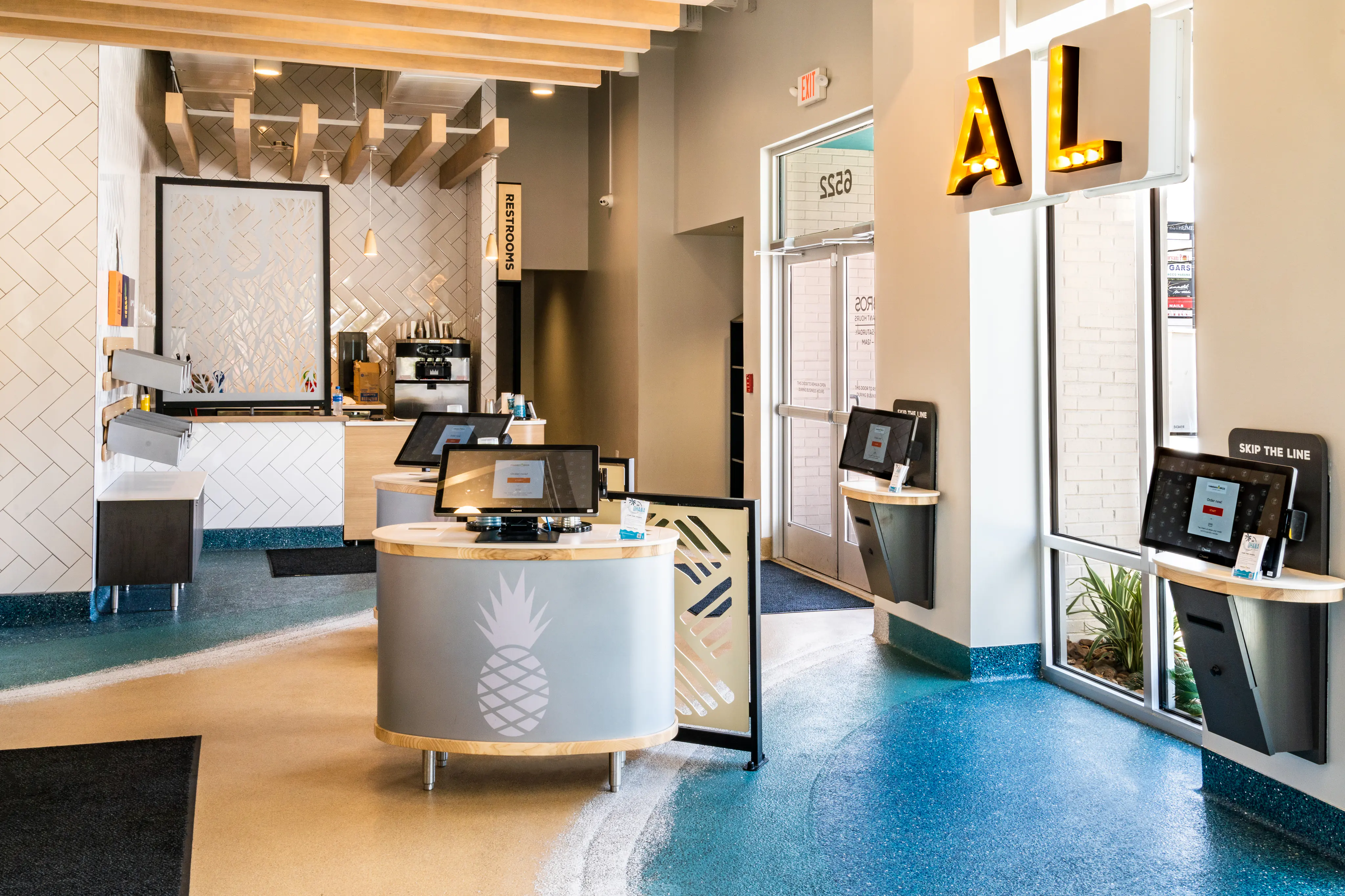 Hawaiian Bros Houston restaurant interior with digital ordering kiosks, a pineapple-branded counter and blue flooring