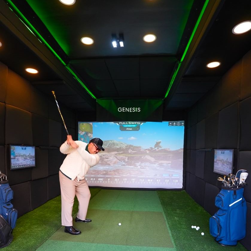 Golfer mid-swing inside the Genesis-branded Dryvebox trailer at a TGL activation with Full Swing simulator screen showing live ball and club tracking data