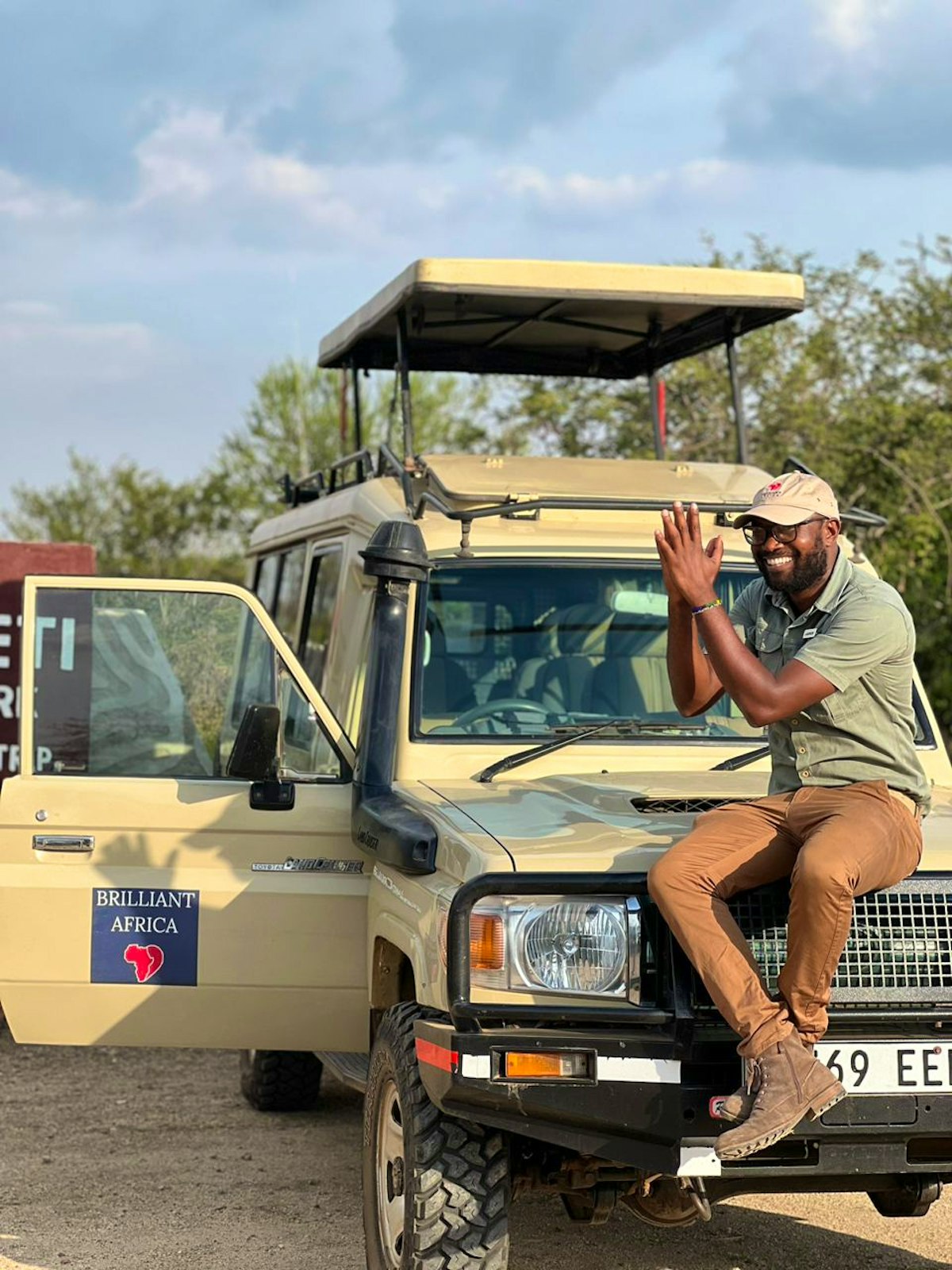 A smiling Brilliant Africa guide beside a branded safari vehicle