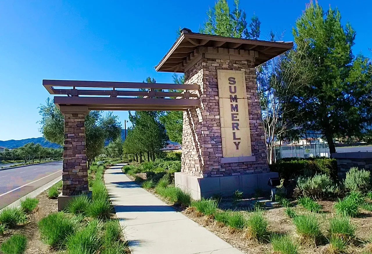 Stone and timber Summerly entry monument beside a landscaped sidewalk in Lake Elsinore, California