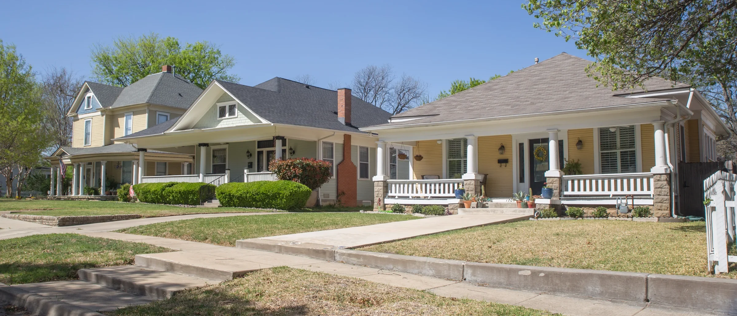Row of Craftsman bungalows with front porches and lawns under a clear sky in Fort Worth's Fairmount Historic District