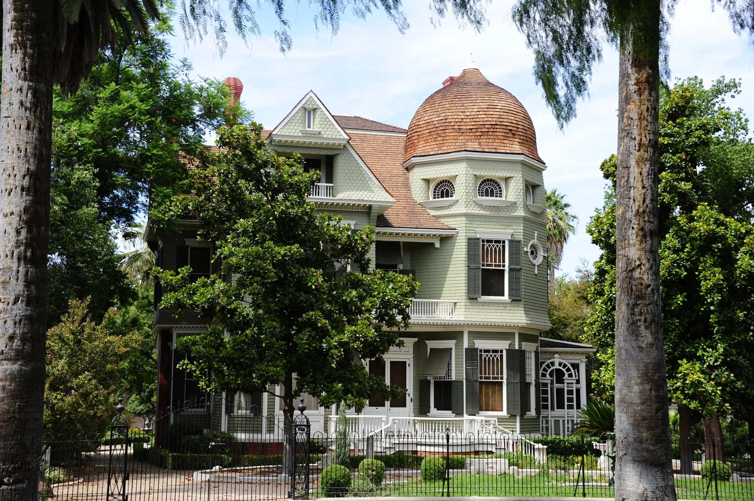 1891 Queen Anne Victorian with a domed turret, framed by palm trunks, on Magnolia Avenue in Riverside