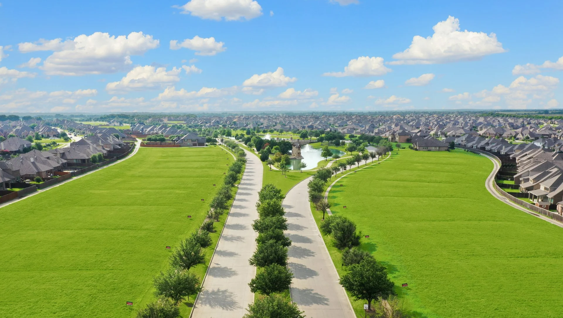 Aerial view of the tree-lined entry boulevard, stone tower pond, and surrounding homes in Devonshire, Forney, Texas