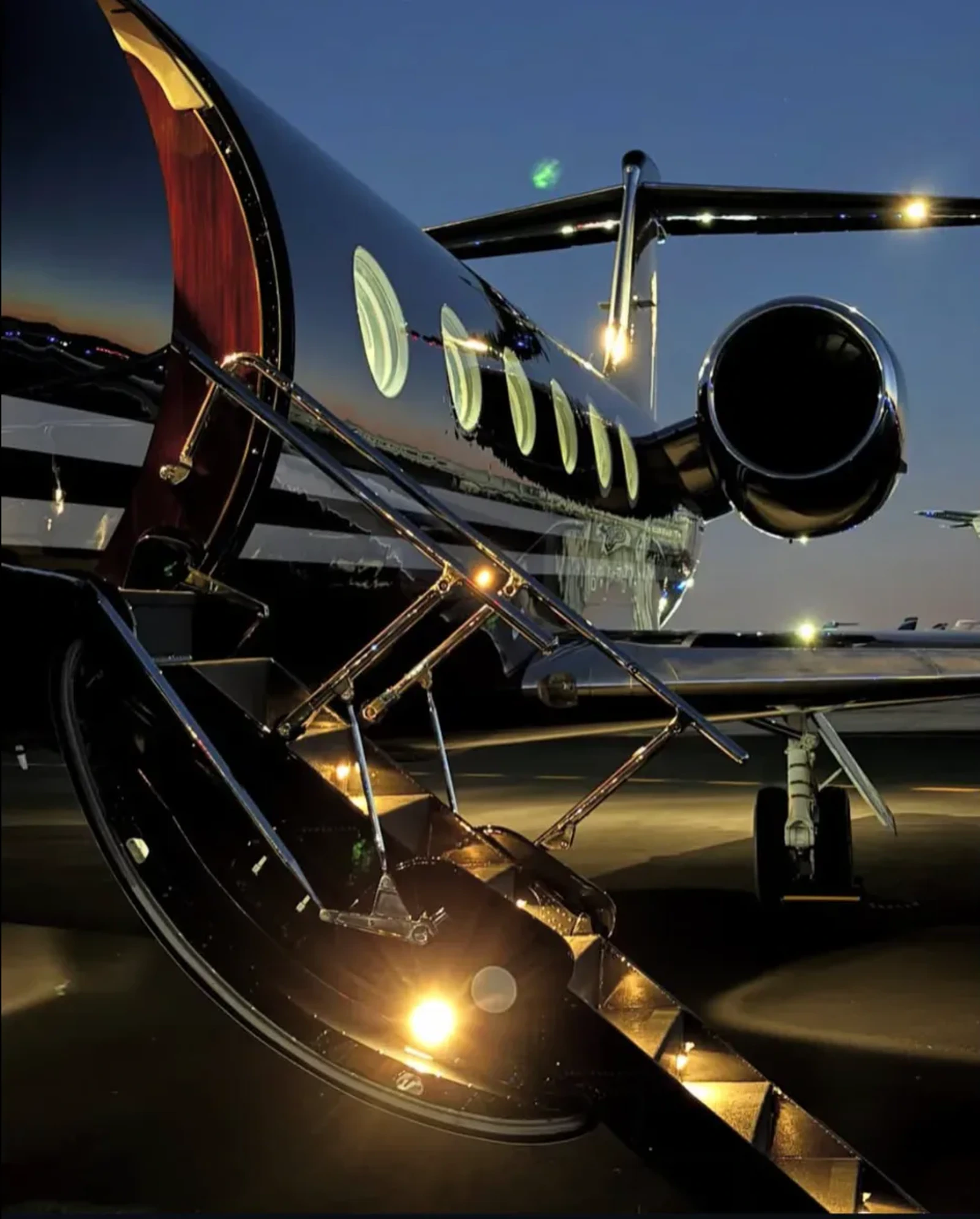 Dark Gulfstream jet with illuminated boarding stairs on a tarmac at night