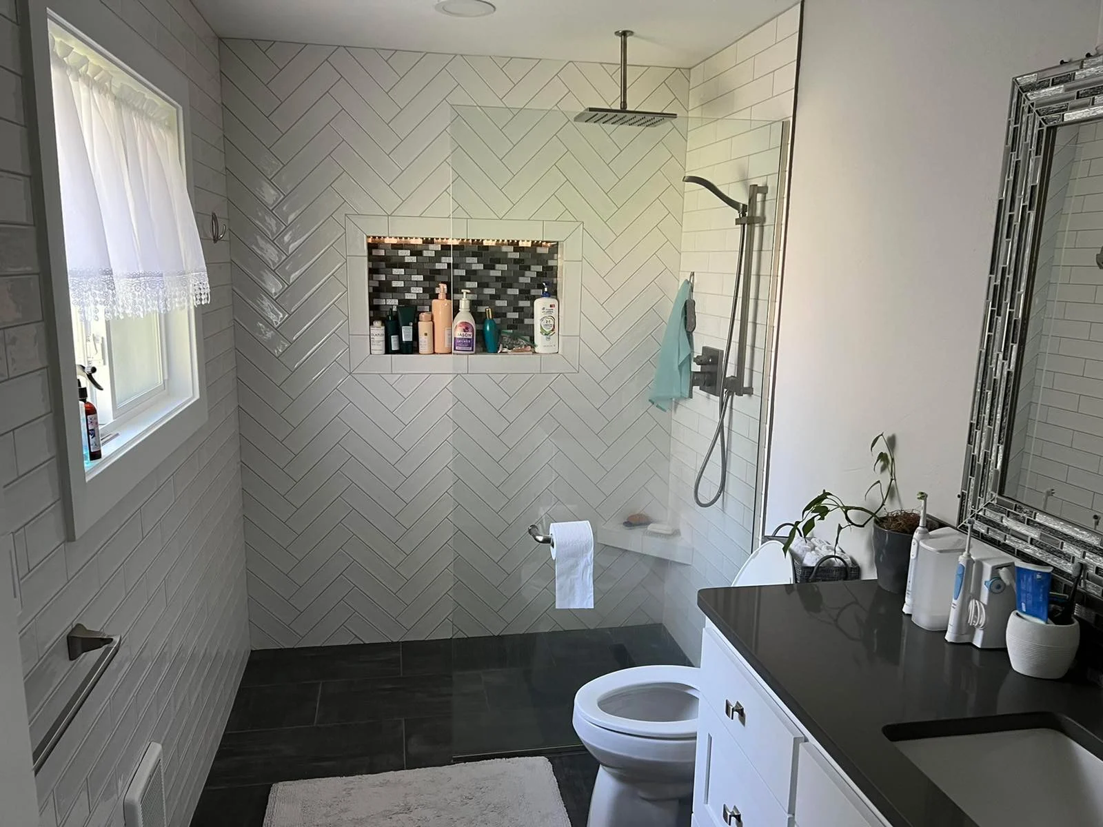 Bathroom with a white herringbone shower wall, tiled niche and dark tile floor