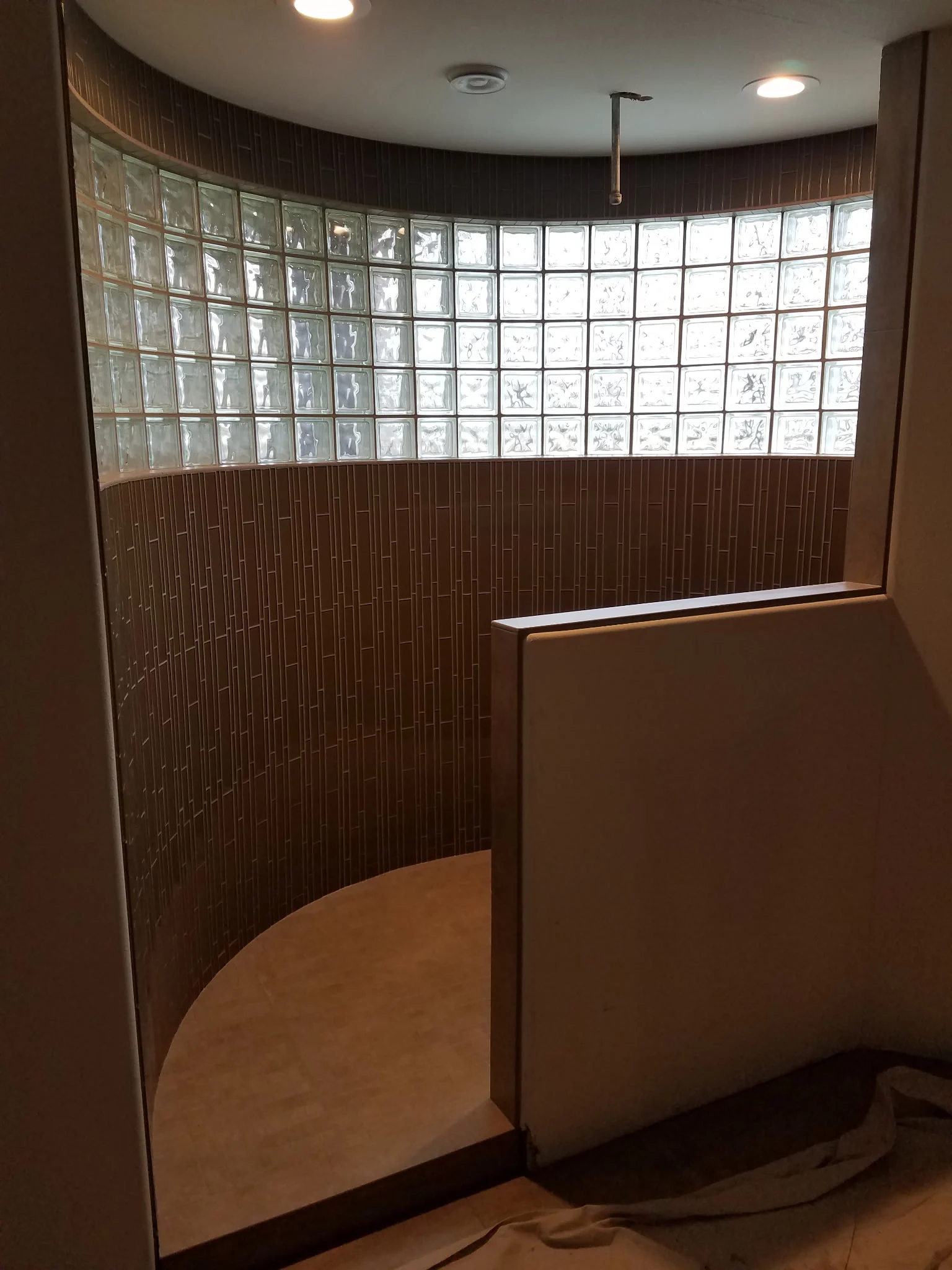 Curved shower with a glass block window band above vertical stacked tile