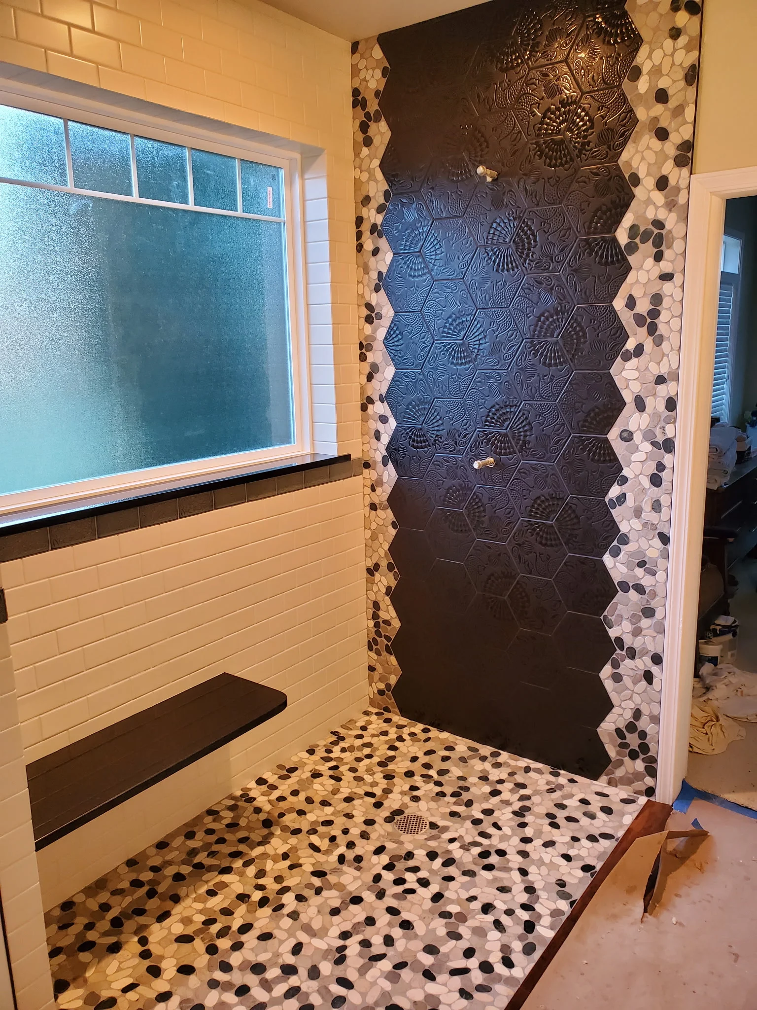 Shower with a dark hexagon feature wall, pebble floor and floating bench
