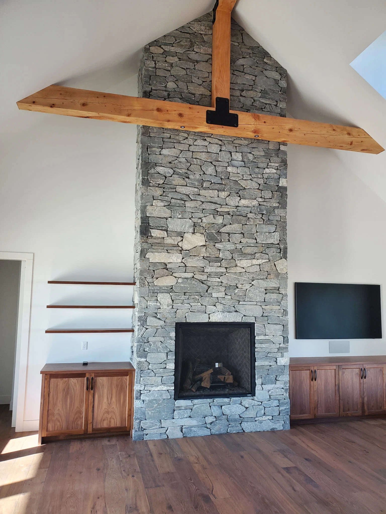 Floor-to-ceiling stone fireplace under a vaulted ceiling with a wood beam