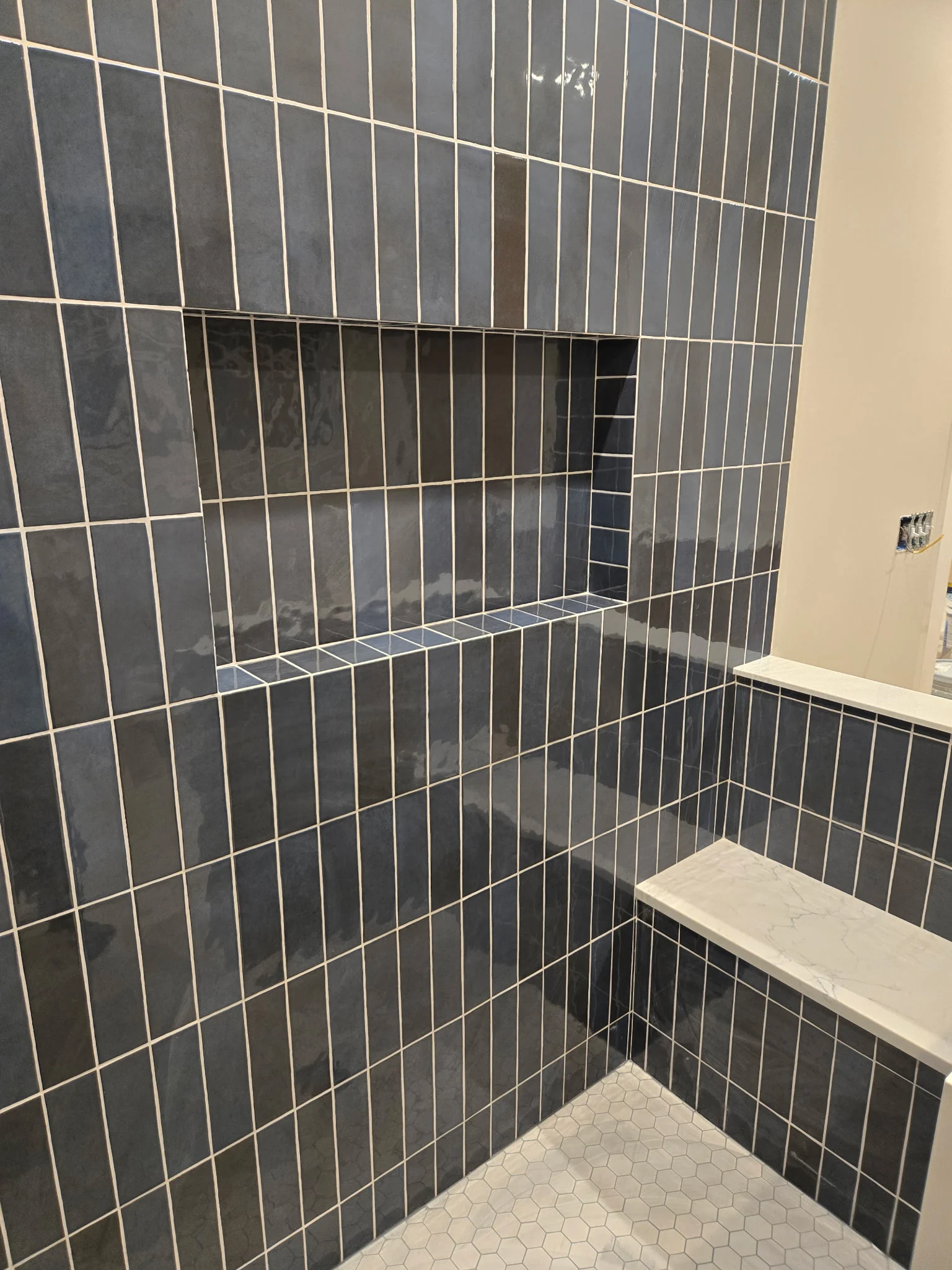 Shower in dark blue vertical tile with a recessed niche and bench