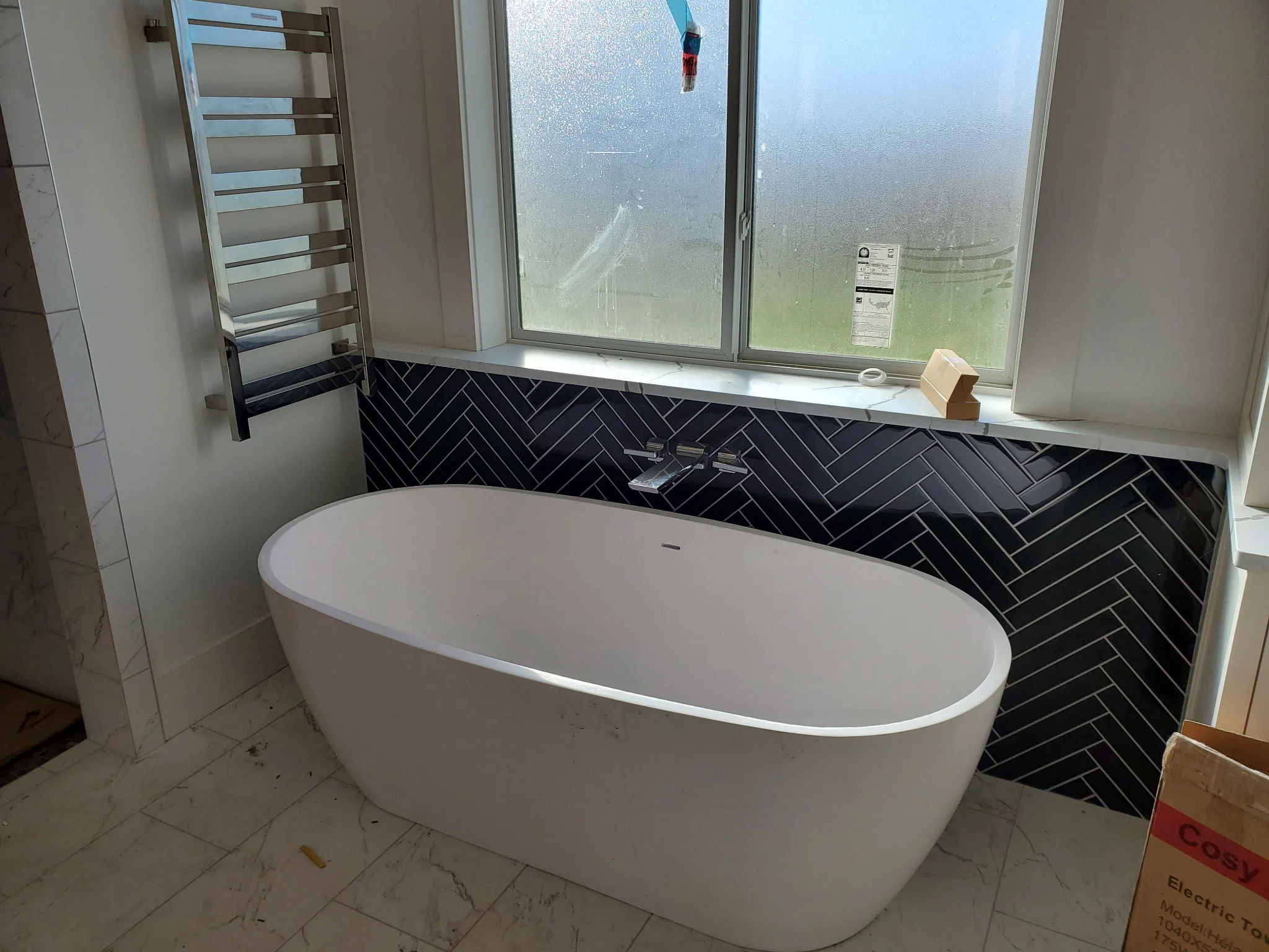 Freestanding tub in front of a dark herringbone tile wall below a window