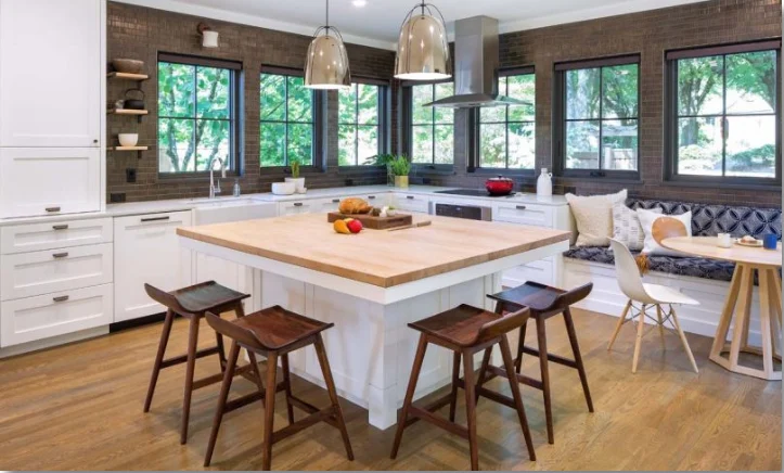 Kitchen with a white island and butcher-block top, bench seating under windows, pendant lights, and dark brick walls