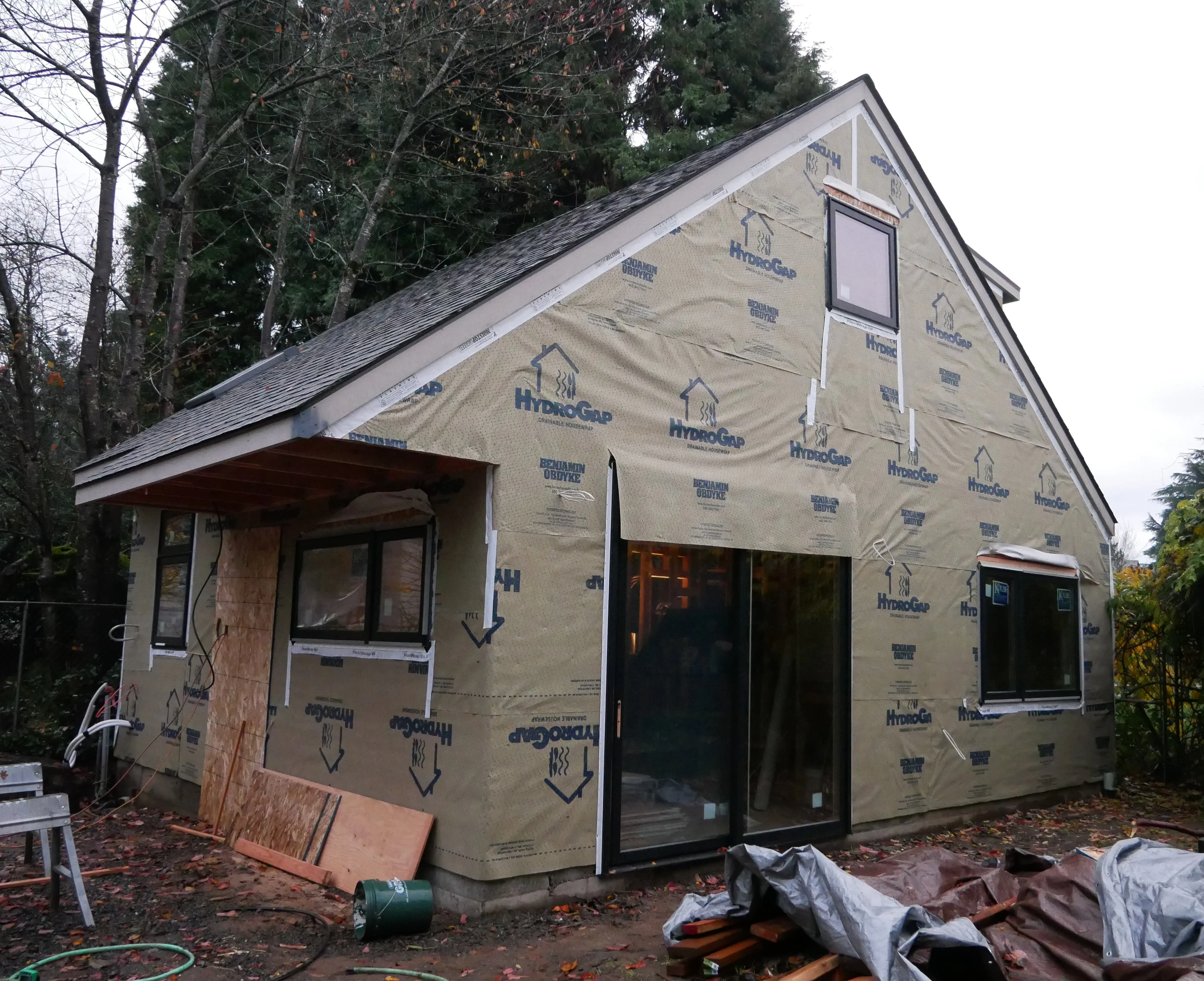 Gable-roofed house wrapped in HydroGap housewrap with new black-framed windows and a sliding door under construction