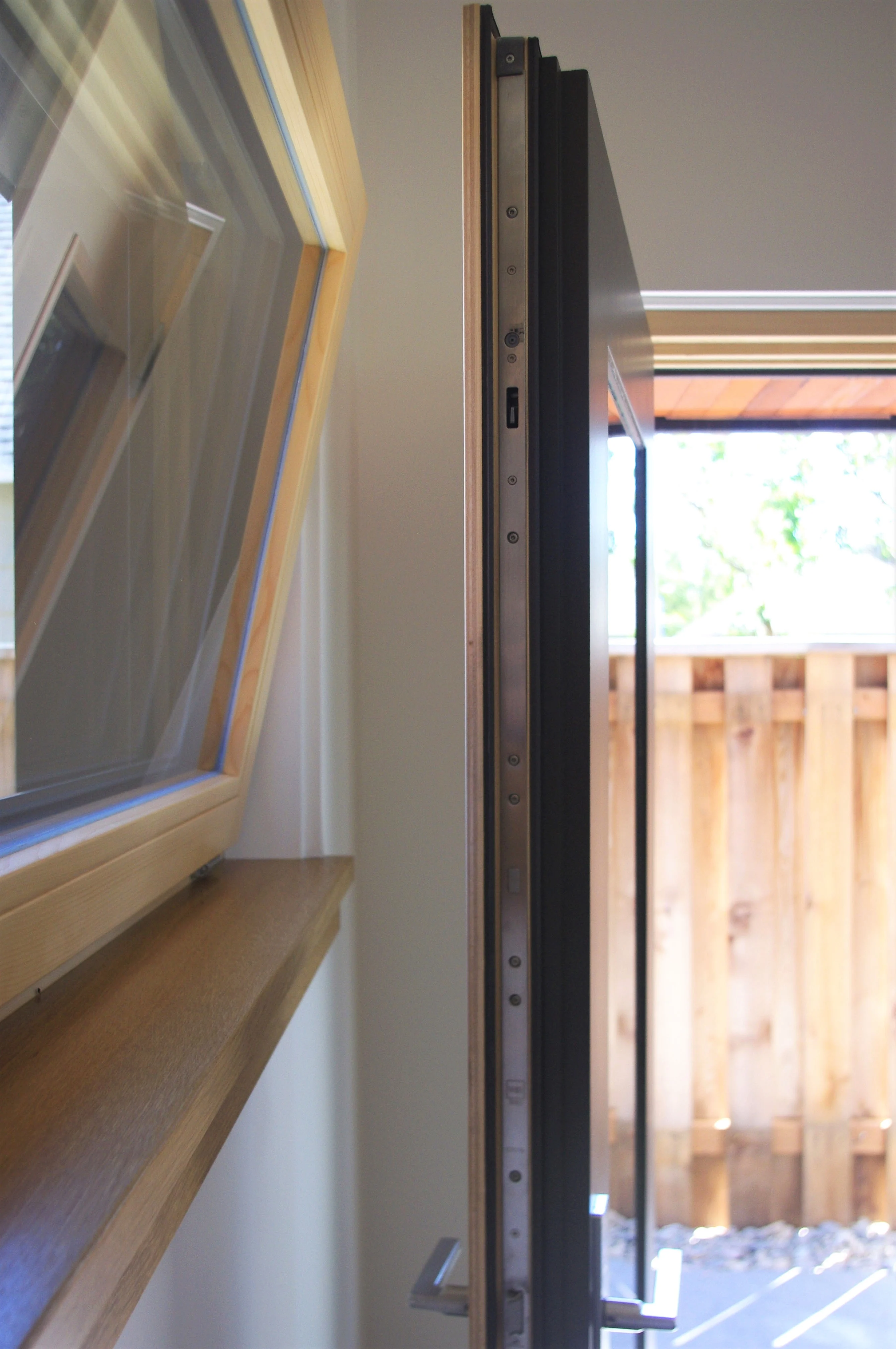 Close-up of a wood-framed window and a dark metal door edge with a multipoint lock, showing the sash and frame profiles