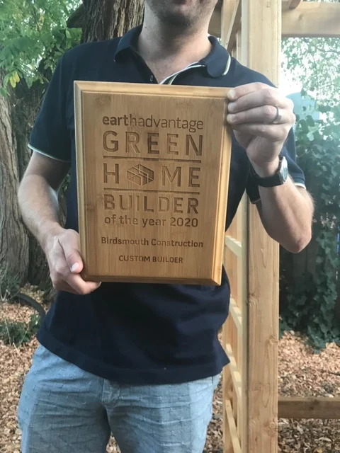 Man in a navy polo holding a wood plaque that reads "earthadvantage GREEN HOME BUILDER of the year 2020" and "CUSTOM BUILDER"