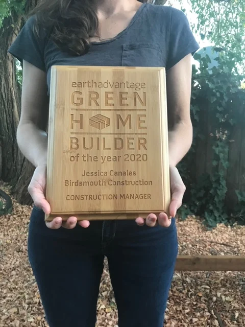 Woman in a gray top holding a wood plaque that names Jessica Canales and reads "CONSTRUCTION MANAGER"