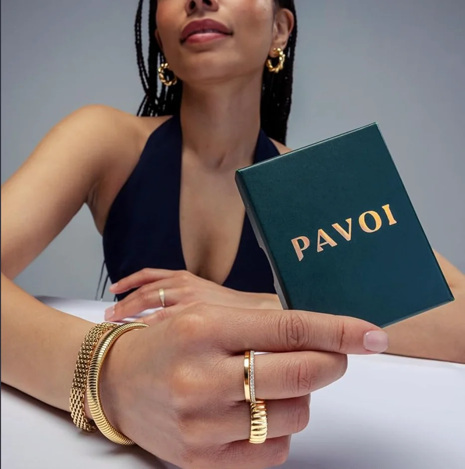 Model holding a green Pavoi gift box, wearing gold rings and bracelets