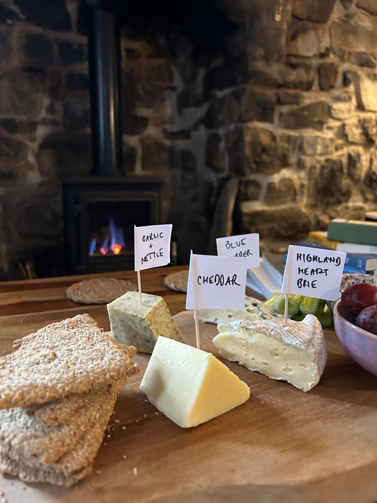 A cheeseboard of labelled Scottish cheeses, oatcakes and grapes in front of the wood-burning stove