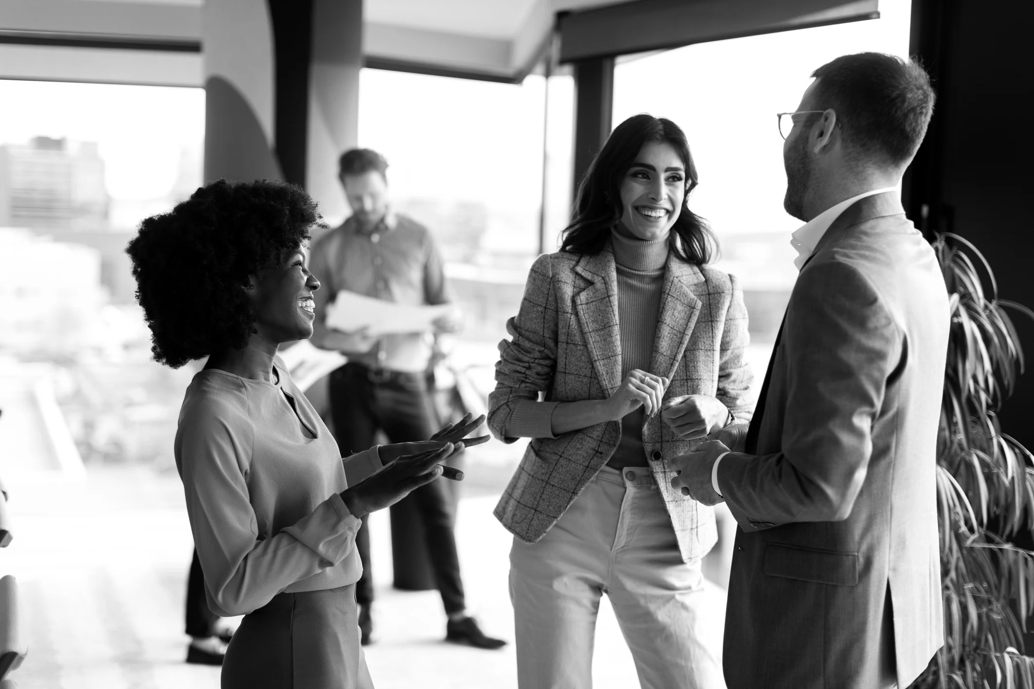 Black-and-white editorial photograph of professionals discussing work in an office.