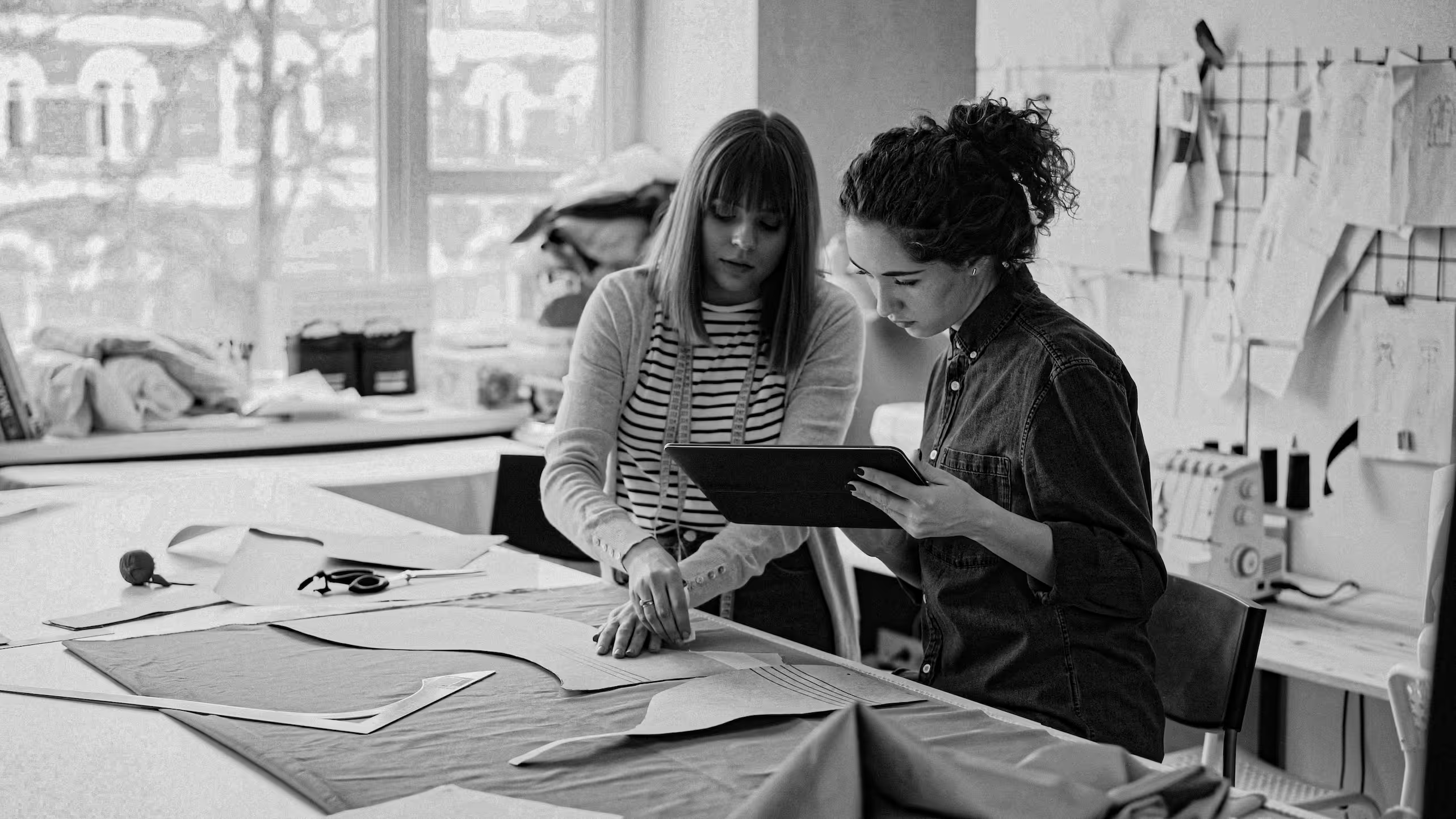 Two women reviewing fabric patterns and a tablet at a worktable in a design studio.