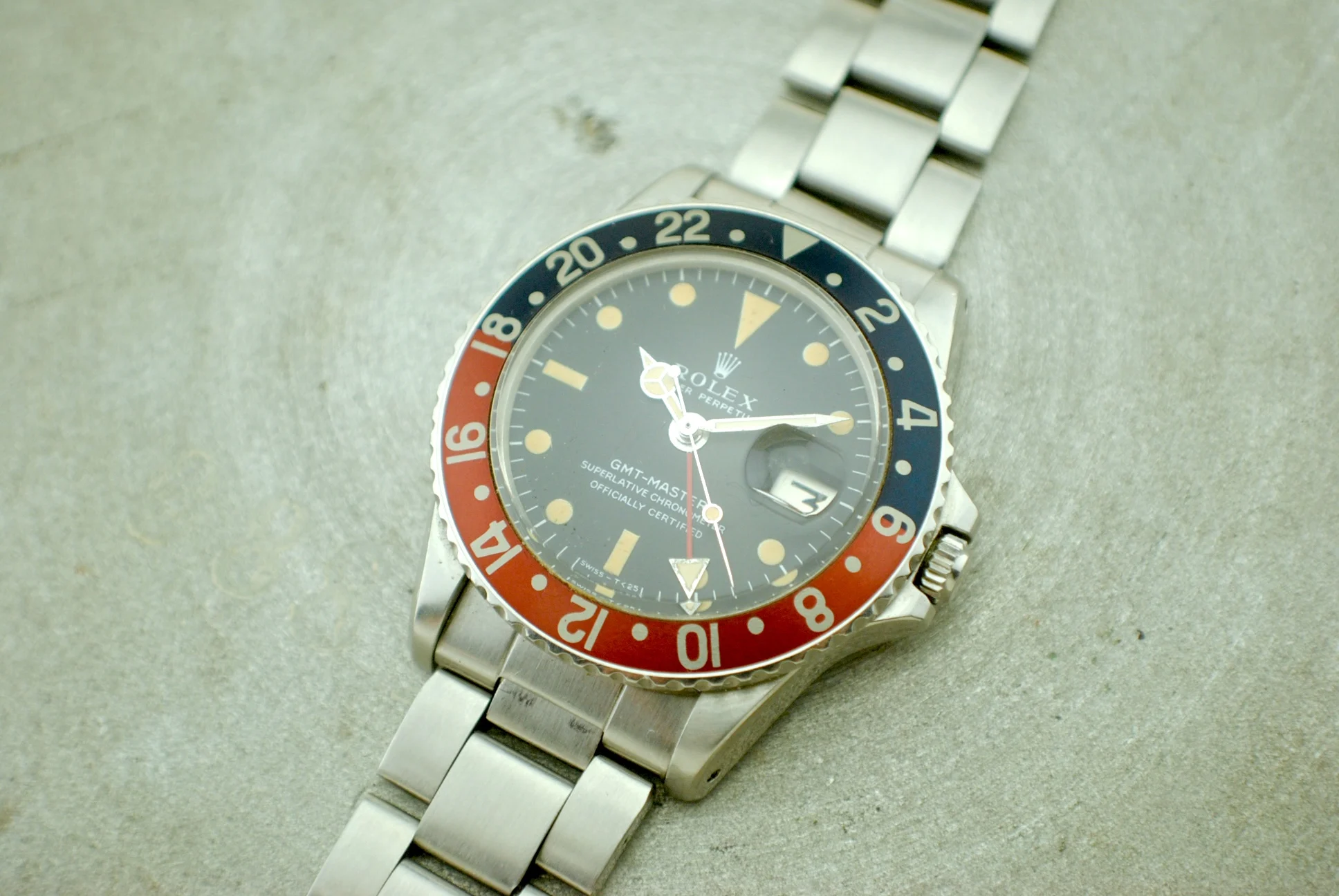 Angled crystal-on view of the Rolex GMT-Master 1675 and its silver-tone three-link bracelet on a pale workshop surface