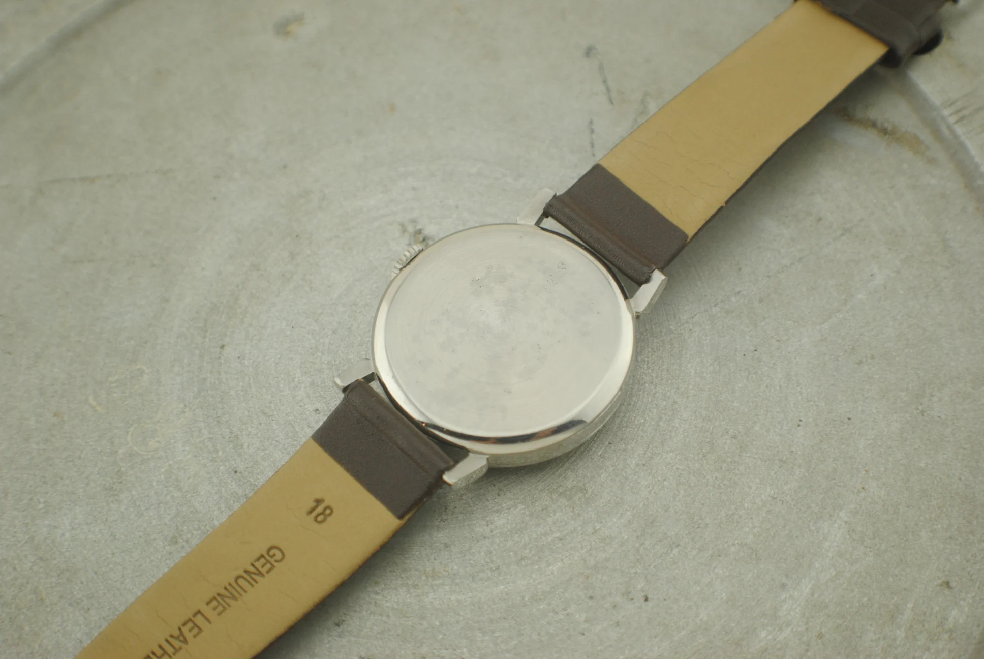 Closed caseback and brown leather strap of the Omega CK2015 Fagiolino on a grey surface