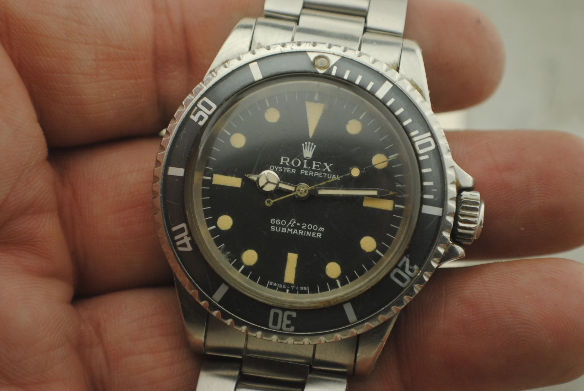 In-hand crystal-on front view of the Rolex Submariner 5513 showing its feet-first dial text, patina, bezel insert and bracelet